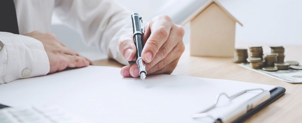 man filing out form with a wooden house and money in the background
